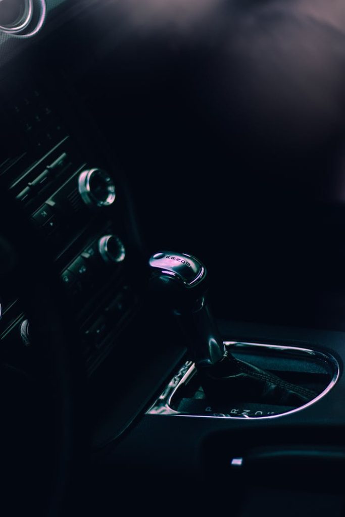 close-up-of-an-automatic-gear-shifter-9403686 Detailed view of a cars gearshift lever in a dimly lit interior setting, featuring modern design.